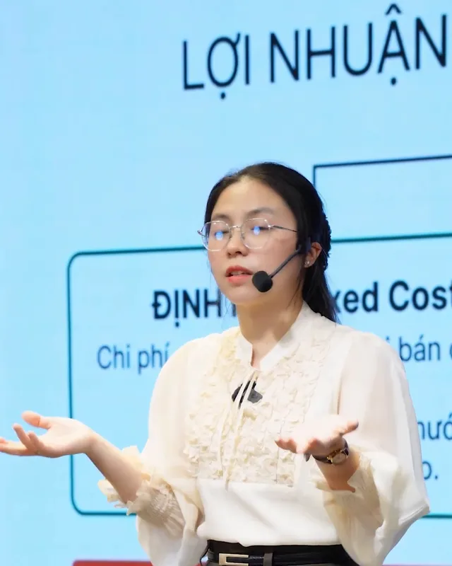 Cô Ly Phạm đứng giảng trước màn chiếu slide "Lợi nhuận" và "Định phí" trong buổi học kinh doanh