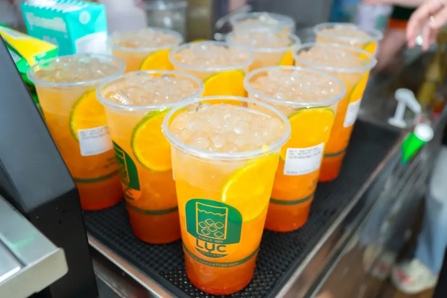 Nhiều ly trà trái cây có logo Lục Coffee & Tea xếp trên quầy
