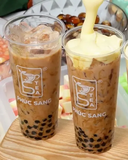 Ly trà sữa trân châu được rót lớp kem phô mai bên khay topping