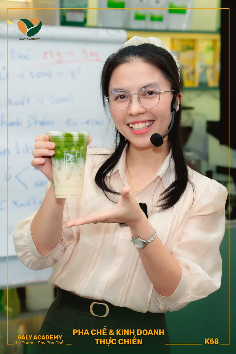 Giảng viên Ly Phạm đeo micro cầm ly thành phẩm hướng dẫn tại lớp pha chế trực tiếp