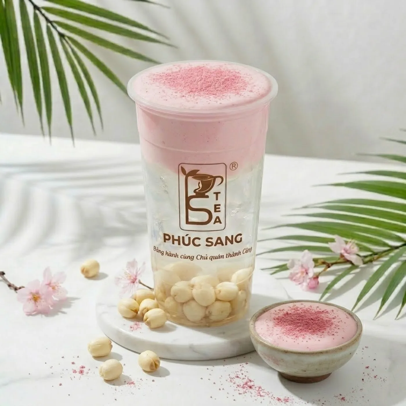 Ly nước dừa kem mây hồng phủ lớp kem hồng mịn, bên cạnh chén hạt sen