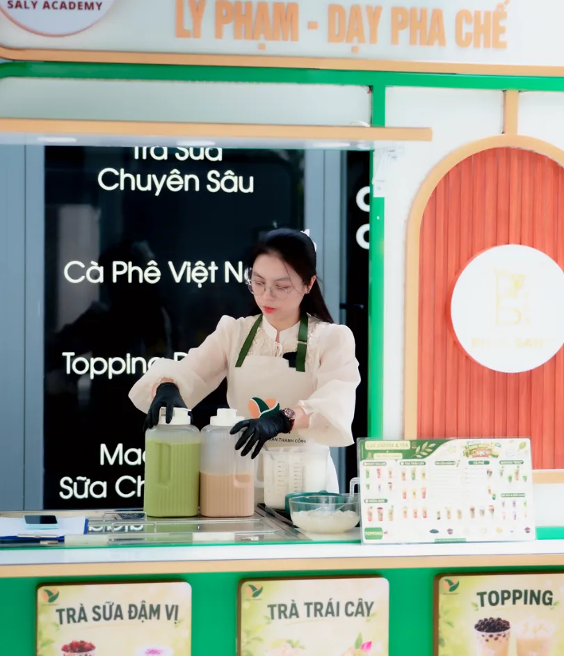 Giảng viên đứng quầy xe trà mẫu tại học viện, màn hình menu trà sữa chuyên sâu